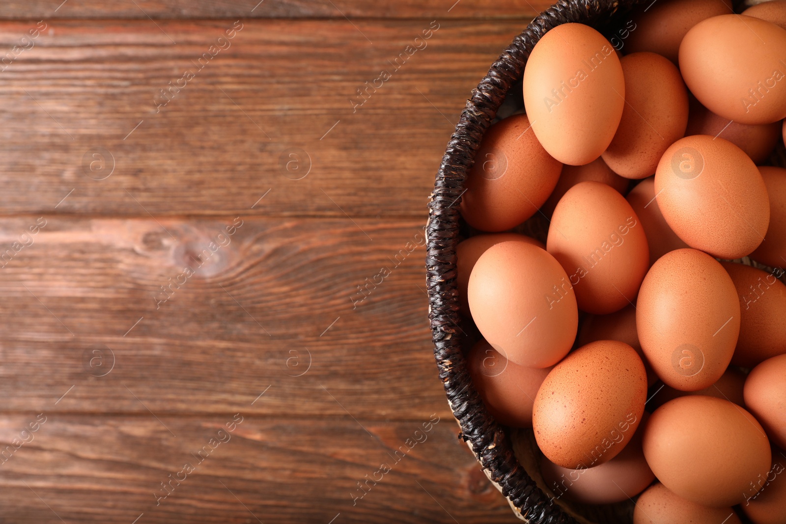 Photo of Raw chicken eggs in wicker basket on wooden table, top view. Space for text