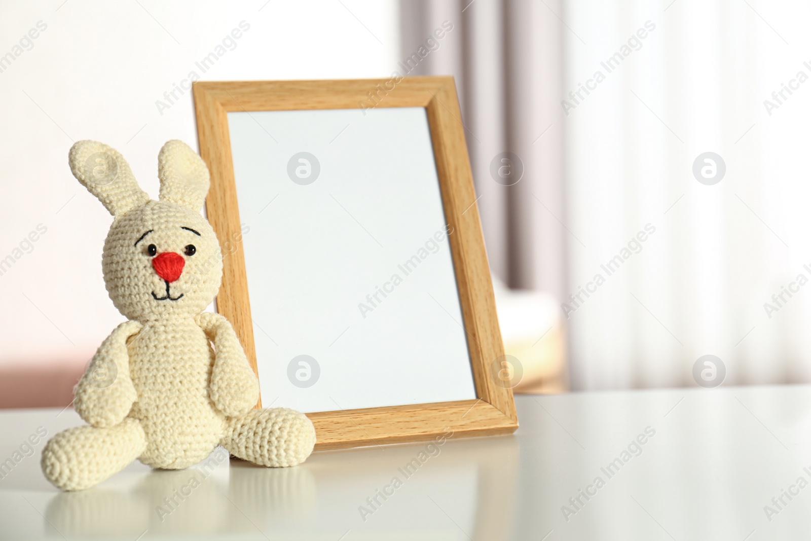 Photo of Photo frame and toy bunny on table in baby room interior. Space for text