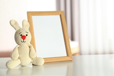 Photo frame and toy bunny on table in baby room interior. Space for text