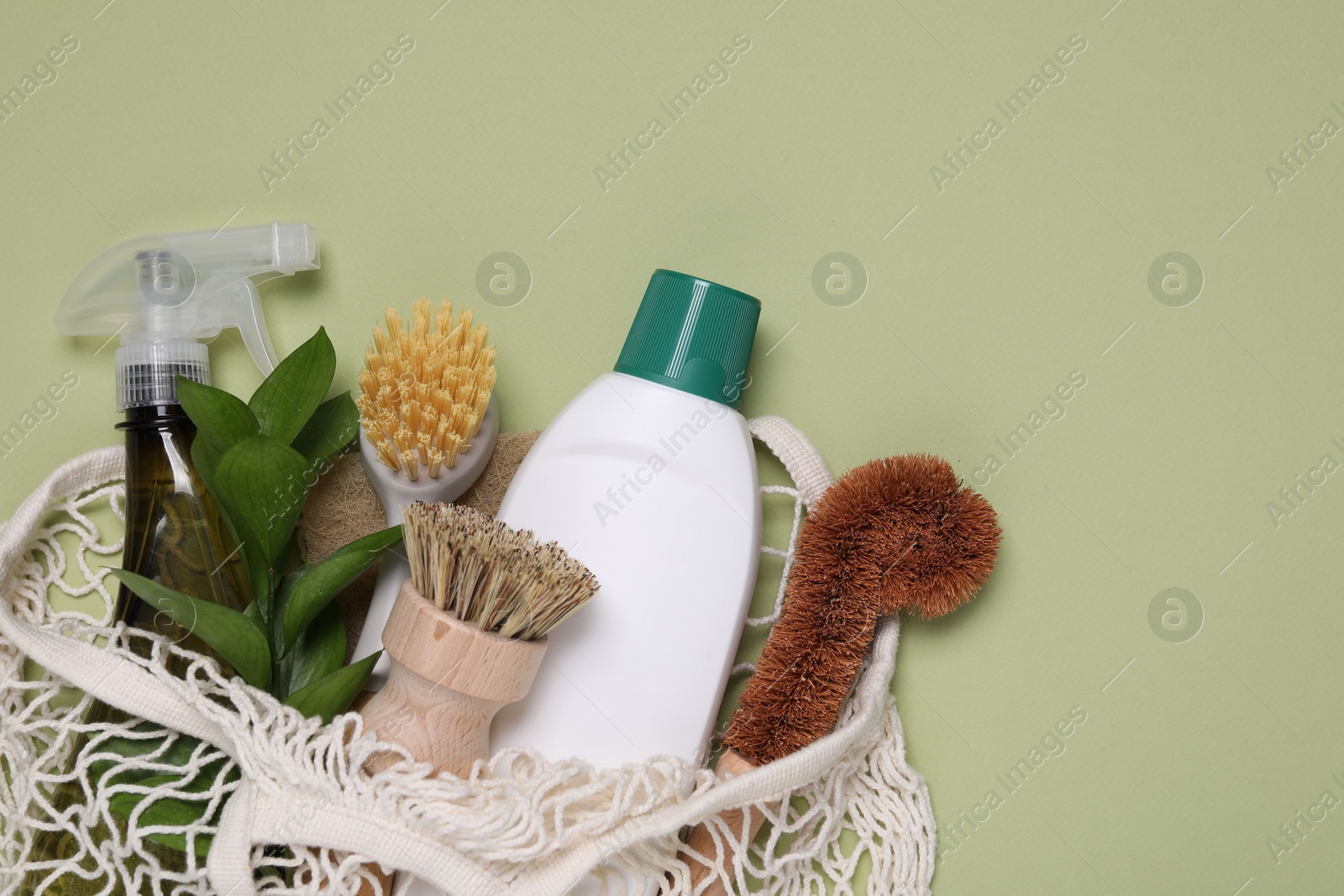 Photo of Different cleaning supplies in string bag on green background, space for text