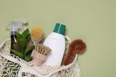 Different cleaning supplies in string bag on green background, space for text