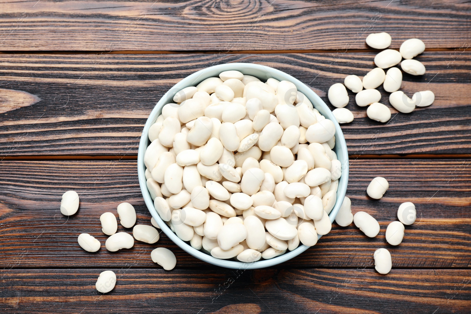 Photo of Raw white beans and bowl on wooden table, flat lay