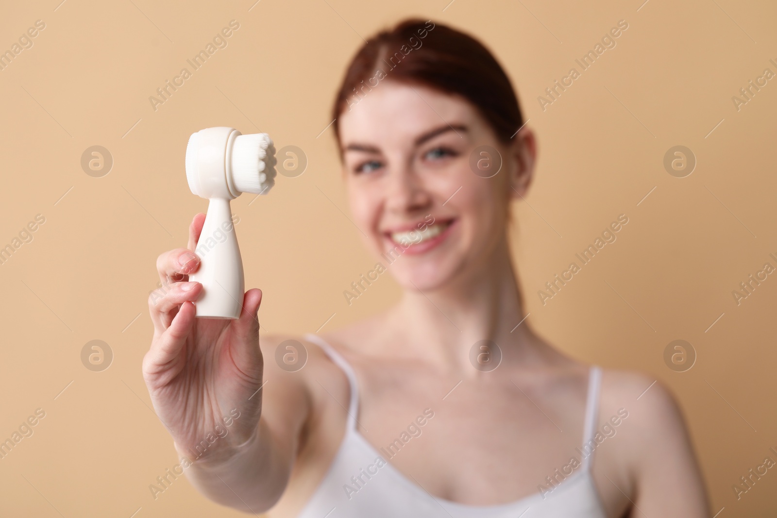 Photo of Washing face. Young woman with cleansing brush on beige background, selective focus