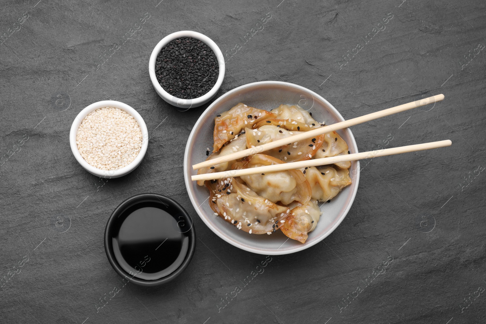 Photo of Delicious gyoza (asian dumplings), soy sauce and sesame seeds on black table, flat lay