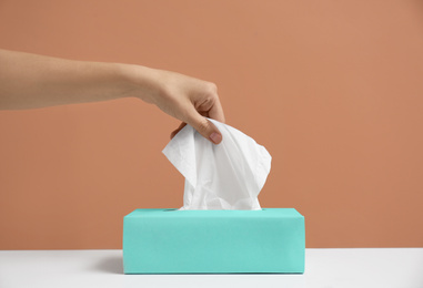 Photo of Woman taking paper tissue from box on light brown background, closeup