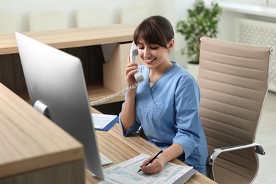 Photo of Smiling medical assistant talking by phone and working with documents in office
