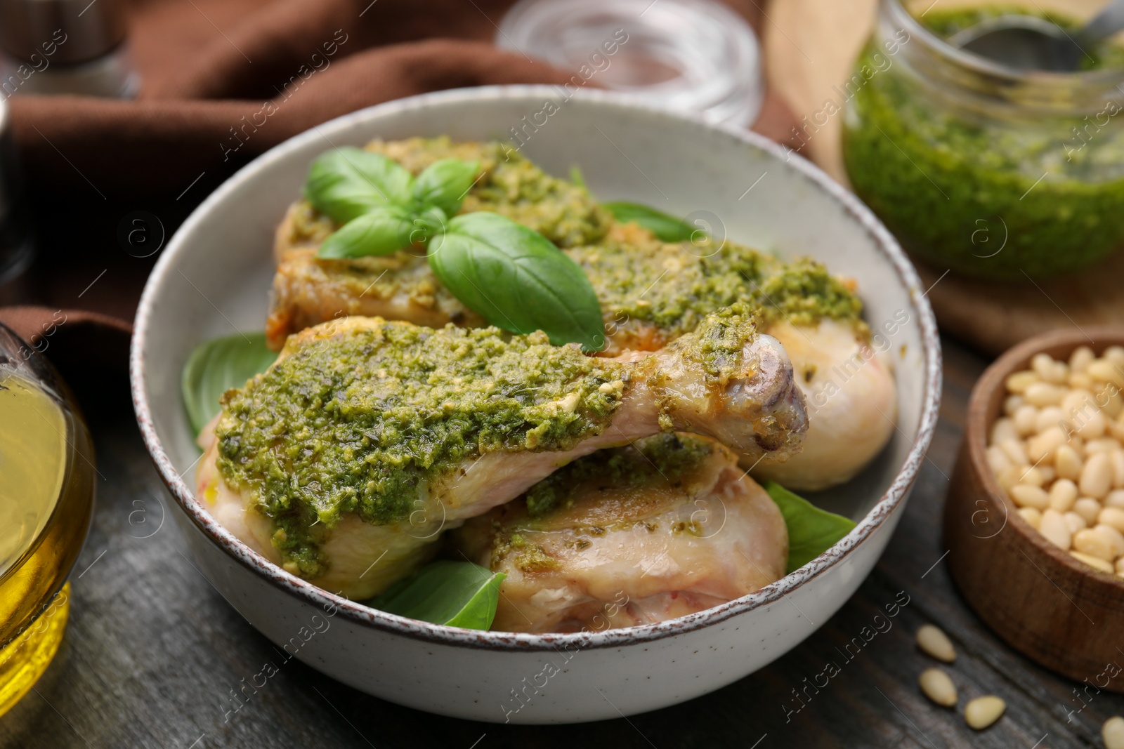 Photo of Delicious fried chicken drumsticks with pesto sauce and basil in bowl on table, closeup