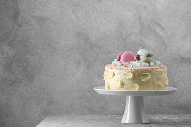 Delicious cake decorated with macarons and marshmallows on grey table, space for text