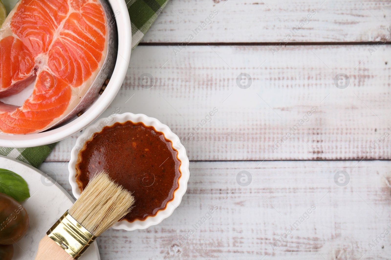 Photo of Fresh marinade, fish and brush on white wooden table, flat lay. Space for text