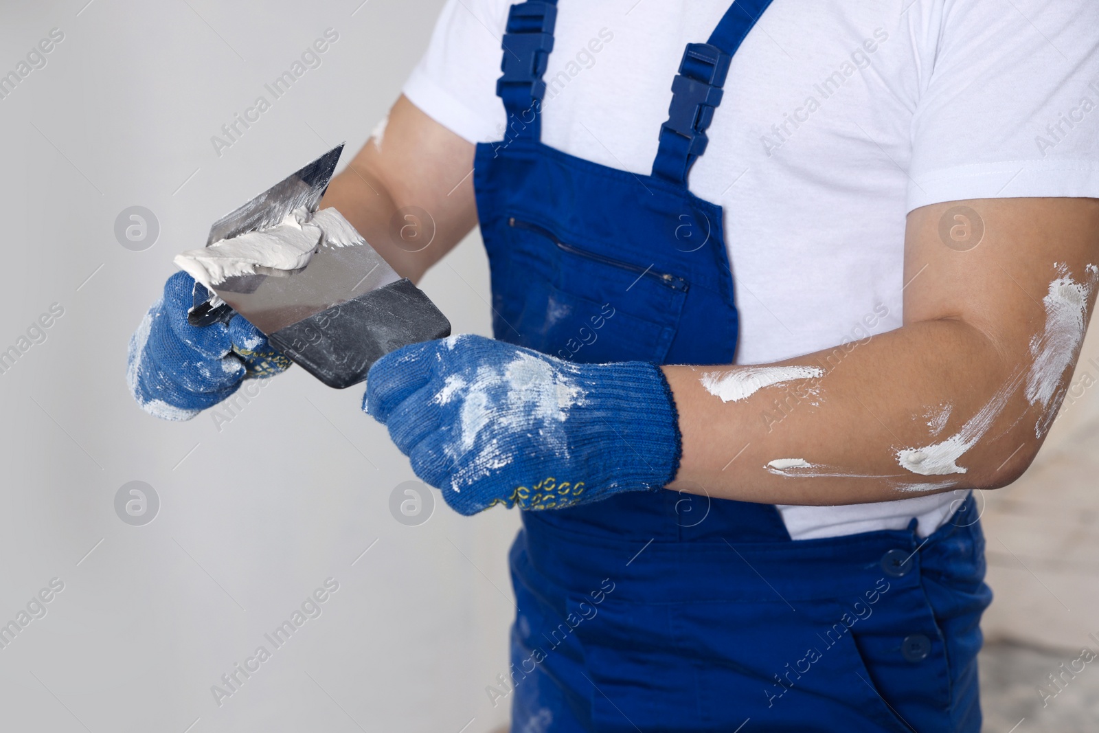 Photo of Worker with putty knives and plaster near wall indoors, closeup. Home renovation