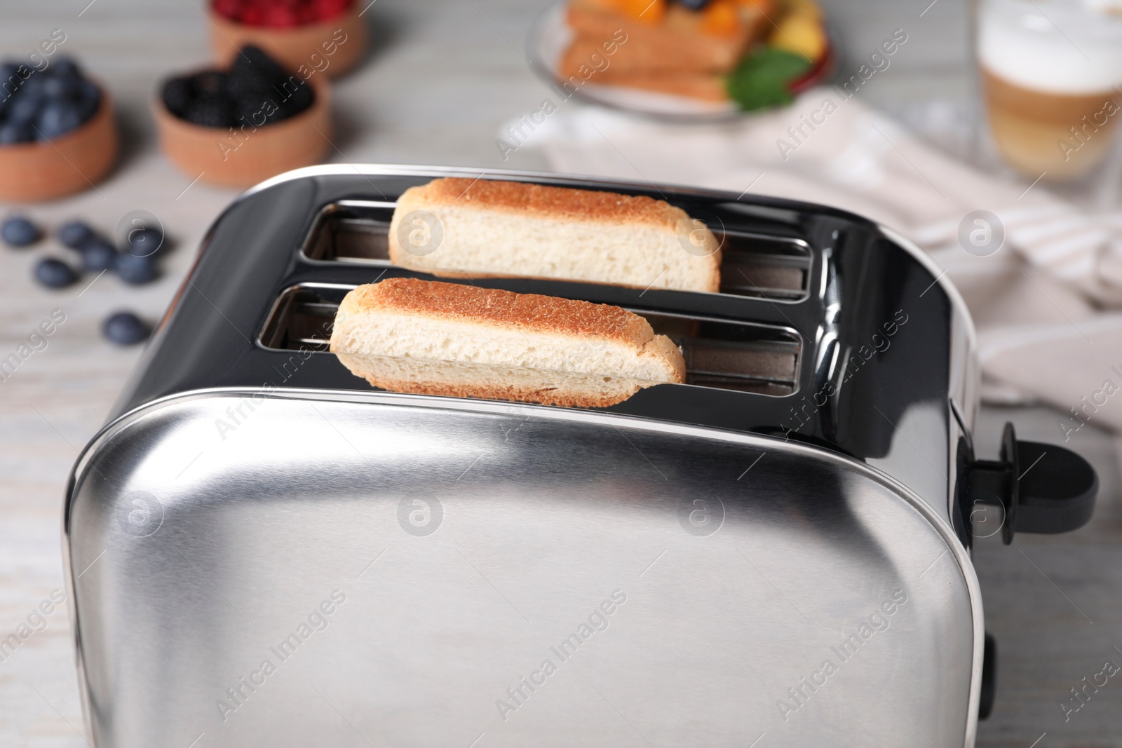 Photo of Modern toaster with bread on white wooden table, closeup