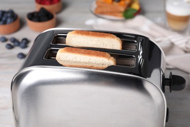Photo of Modern toaster with bread on white wooden table, closeup