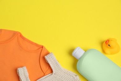 Photo of Bottles of laundry detergents, baby clothes and rubber duck on yellow background, flat lay. Space for text
