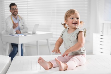 Photo of Pediatrician working at table in clinic, focus on cute little baby