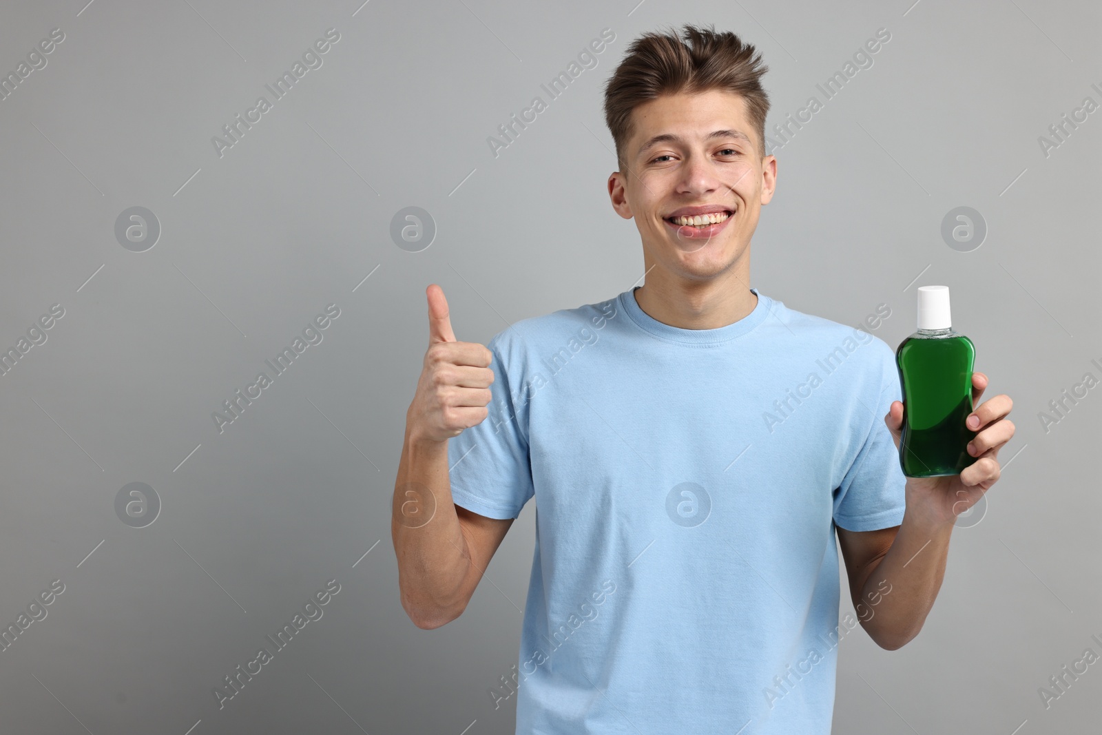 Photo of Young man with mouthwash showing thumbs up on light grey background, space for text