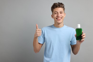 Photo of Young man with mouthwash showing thumbs up on light grey background, space for text