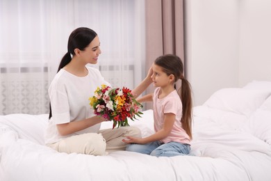 Photo of Happy woman with her daughter and bouquet of lilies on bed at home. Mother's day celebration