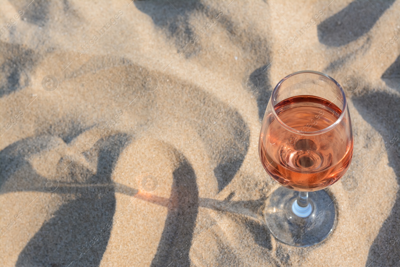 Photo of Glass of tasty rose wine on sand, space for text