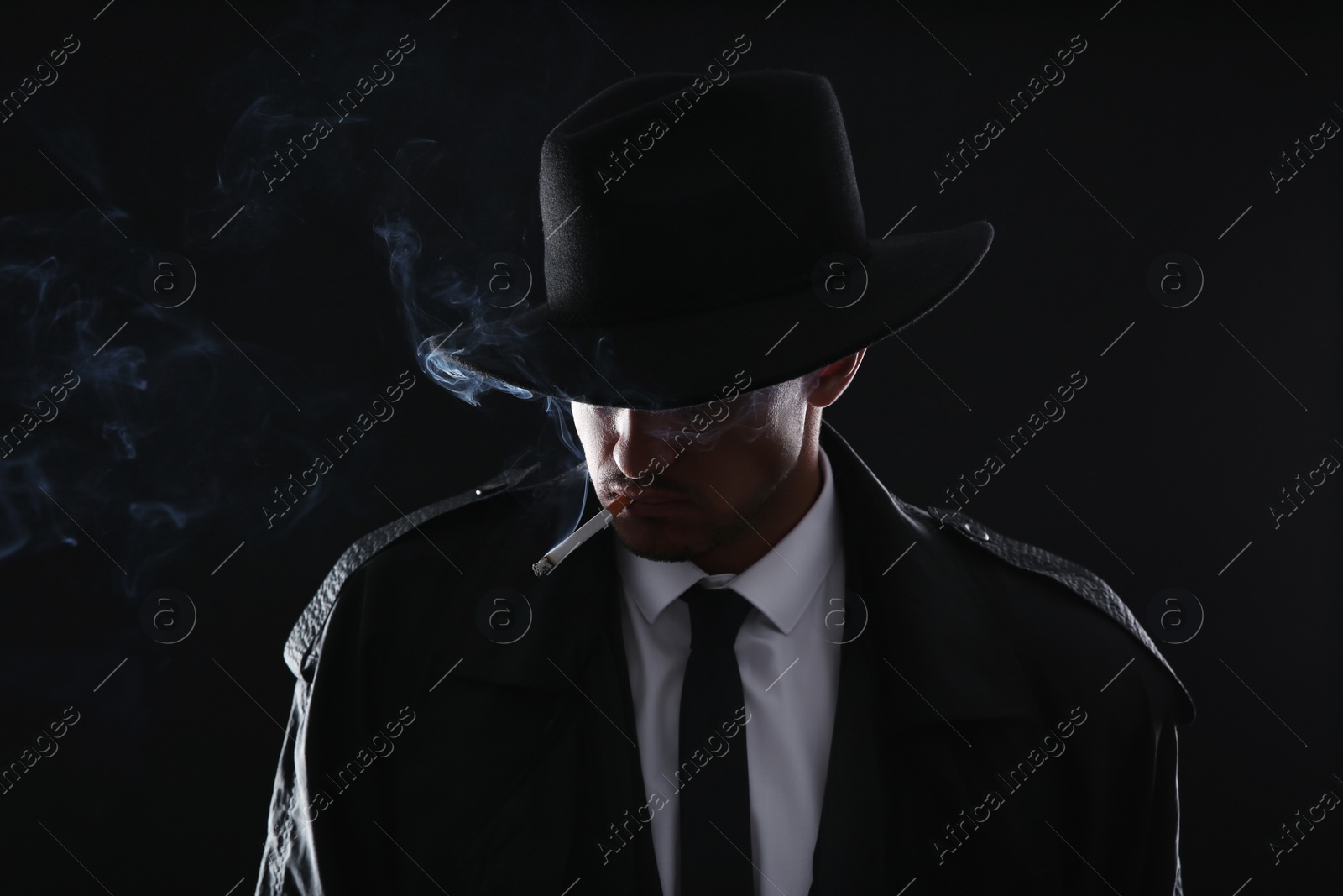 Photo of Old fashioned detective smoking cigarette on dark background