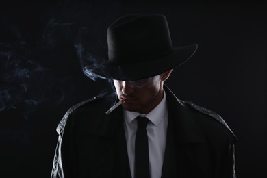 Photo of Old fashioned detective smoking cigarette on dark background