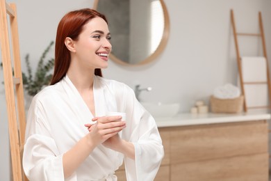 Beautiful young woman applying body cream onto hands in bathroom, space for text
