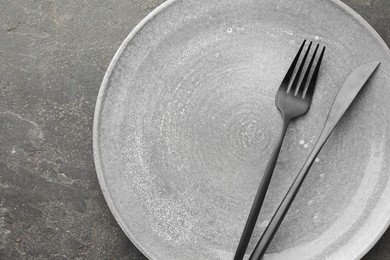 Photo of Clean plate, fork and knife on grey textured table, top view