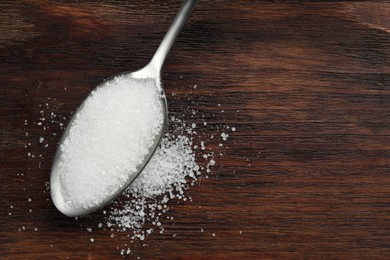 Photo of Spoon with granulated sugar on wooden table, top view. Space for text