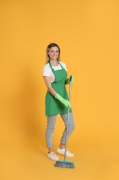 Young woman with broom on orange background