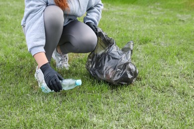 Photo of Woman with trash bag picking up plastic bottle outdoors, closeup. Recycling concept