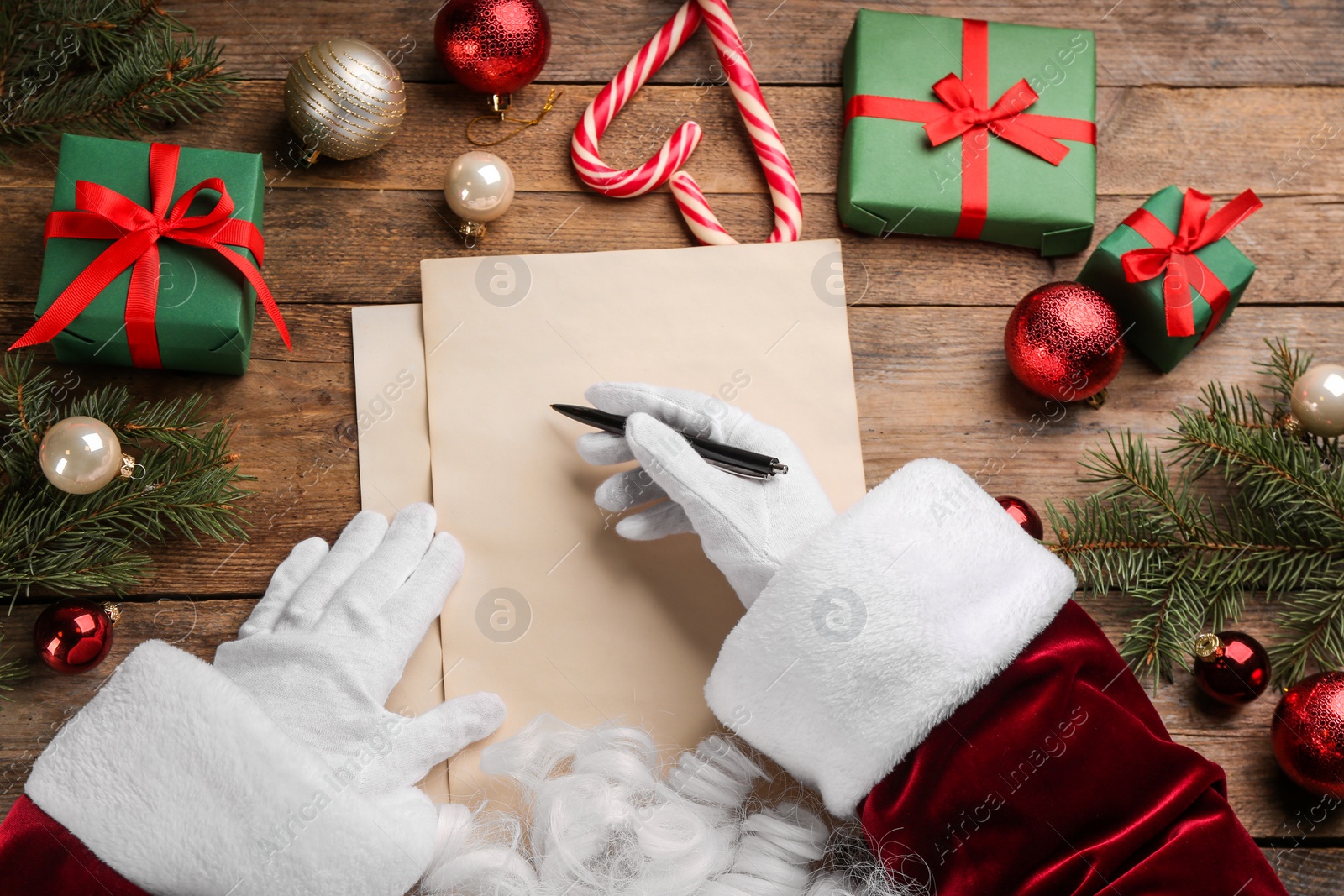 Photo of Santa Claus writing letter at wooden table, top view. Christmas celebration