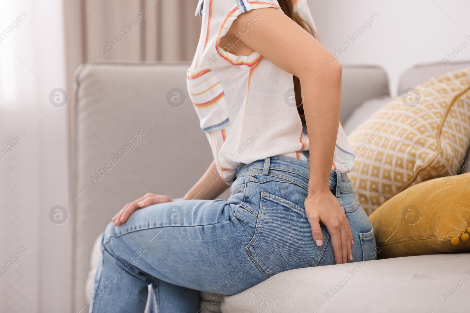 Photo of Young woman suffering from hemorrhoid on sofa at home, closeup