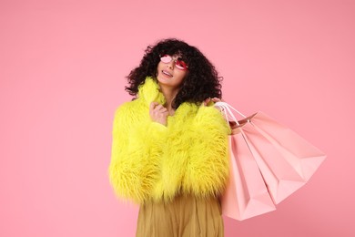 Happy young woman with shopping bags on pink background