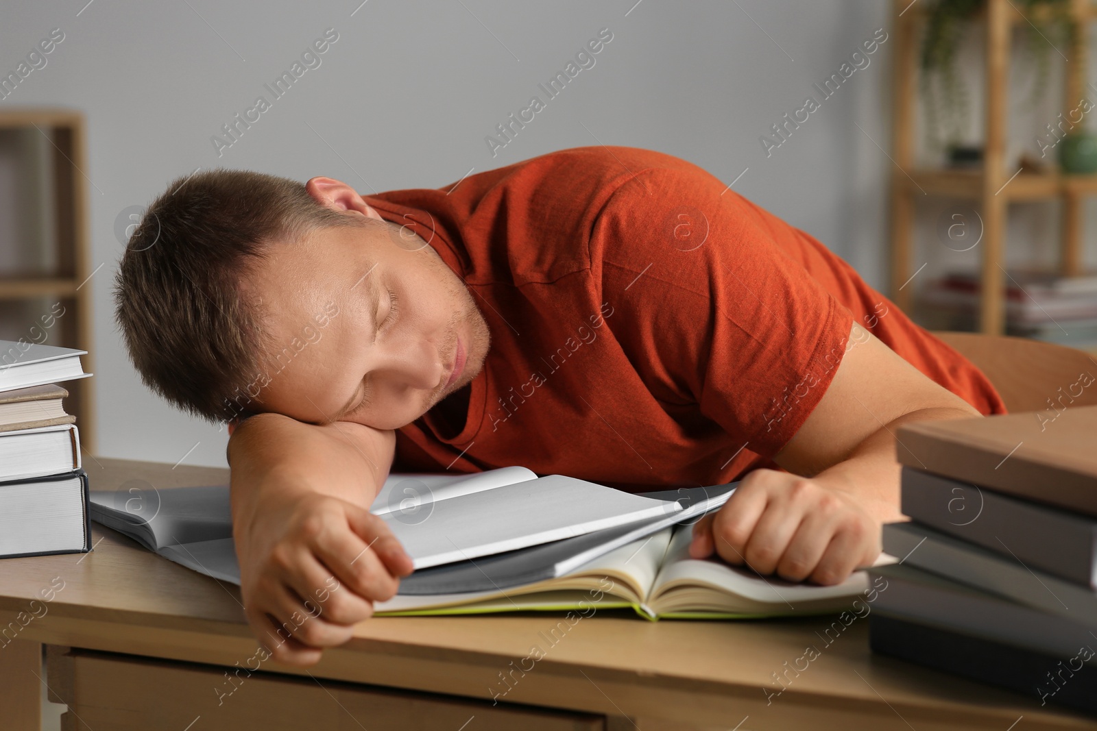 Photo of Tired man sleeping near books at wooden table indoors