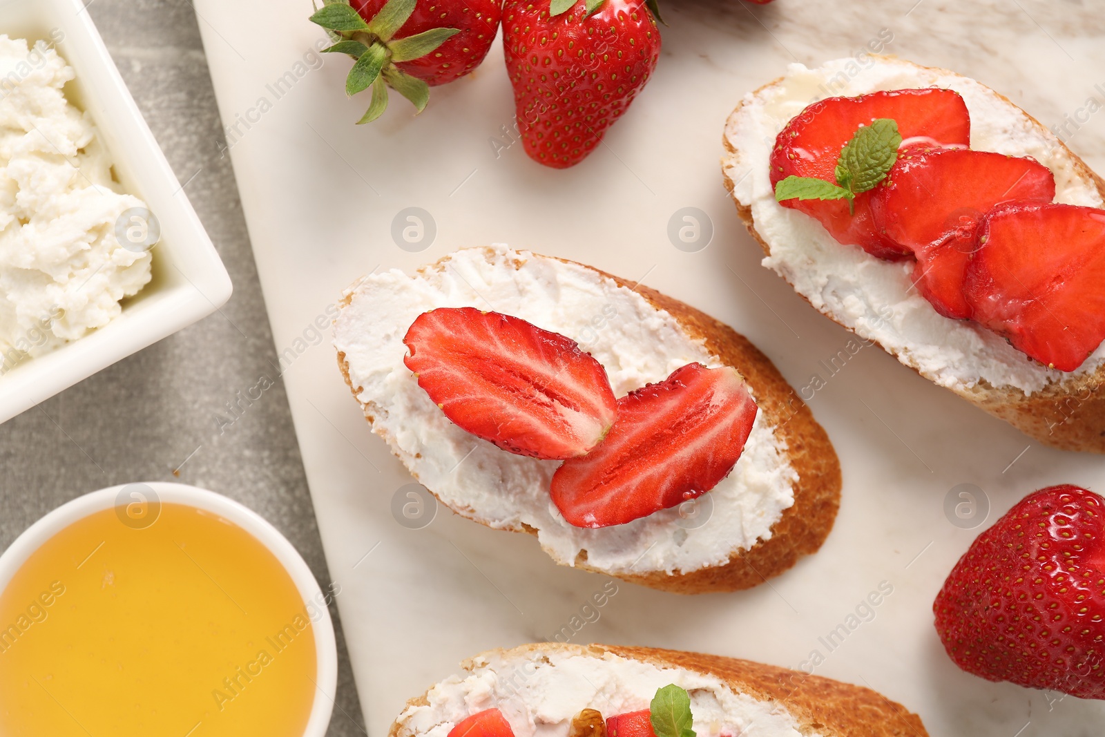 Photo of Delicious ricotta bruschettas with strawberry and mint on grey table, flat lay