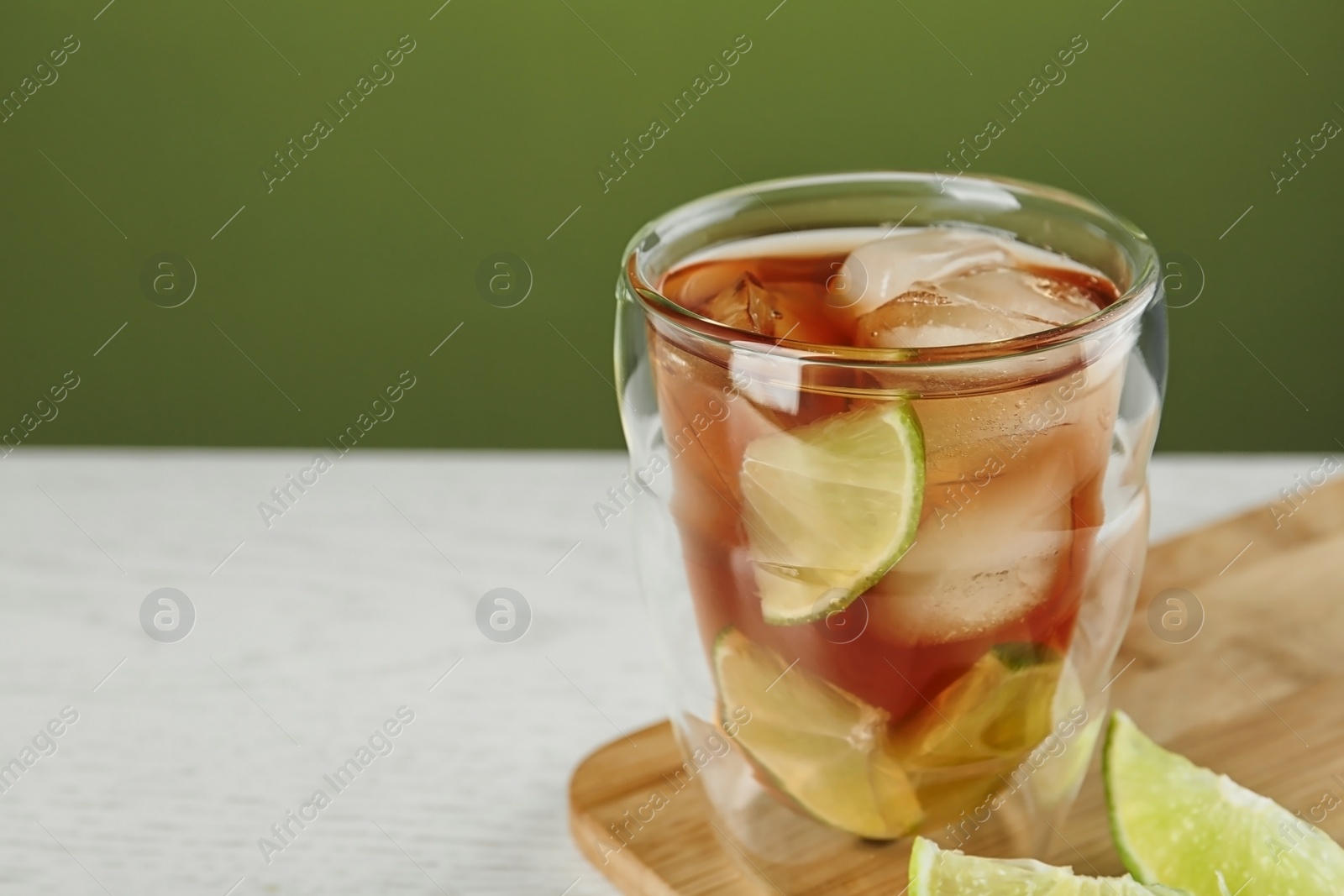 Photo of Glass of tasty ice tea with lime on white wooden table against green background, space for text