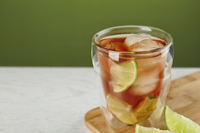 Photo of Glass of tasty ice tea with lime on white wooden table against green background, space for text