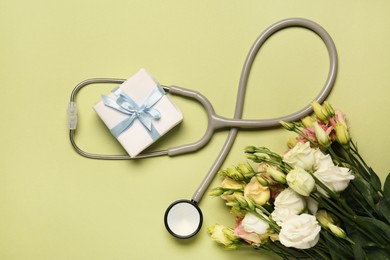 Photo of Stethoscope, gift box and eustoma flowers on light green background, flat lay. Happy Doctor's Day