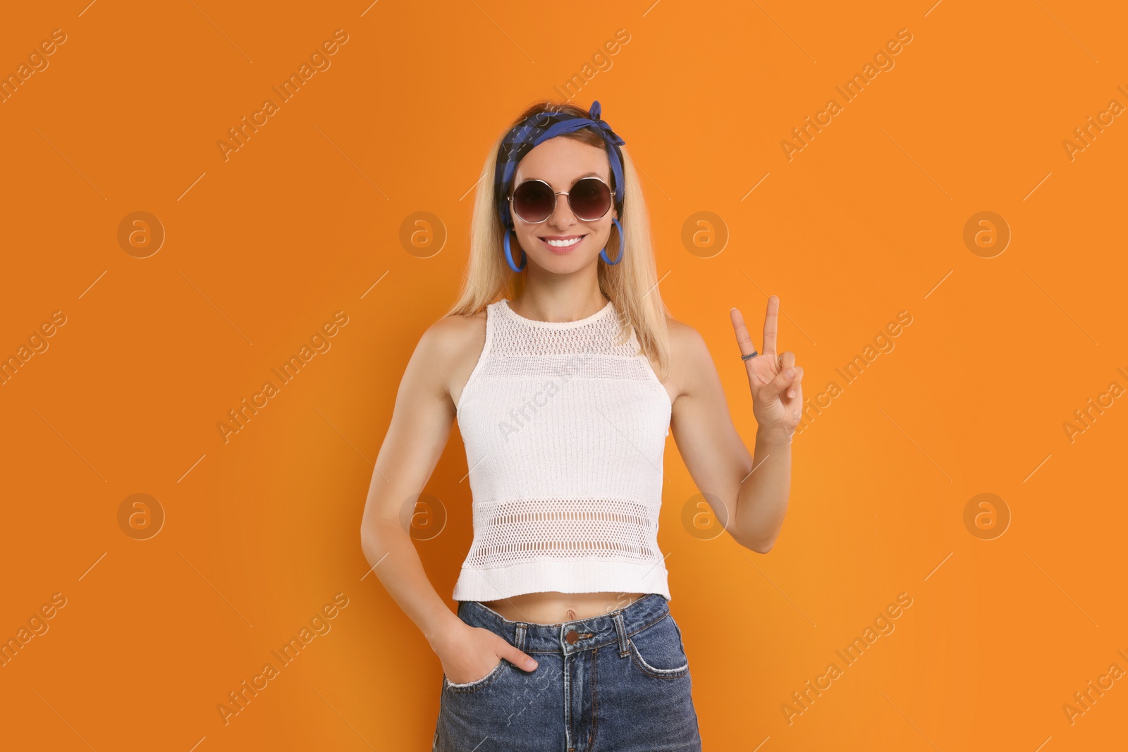 Photo of Smiling hippie woman showing peace sign on orange background