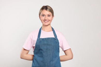 Beautiful young woman in denim apron on light grey background