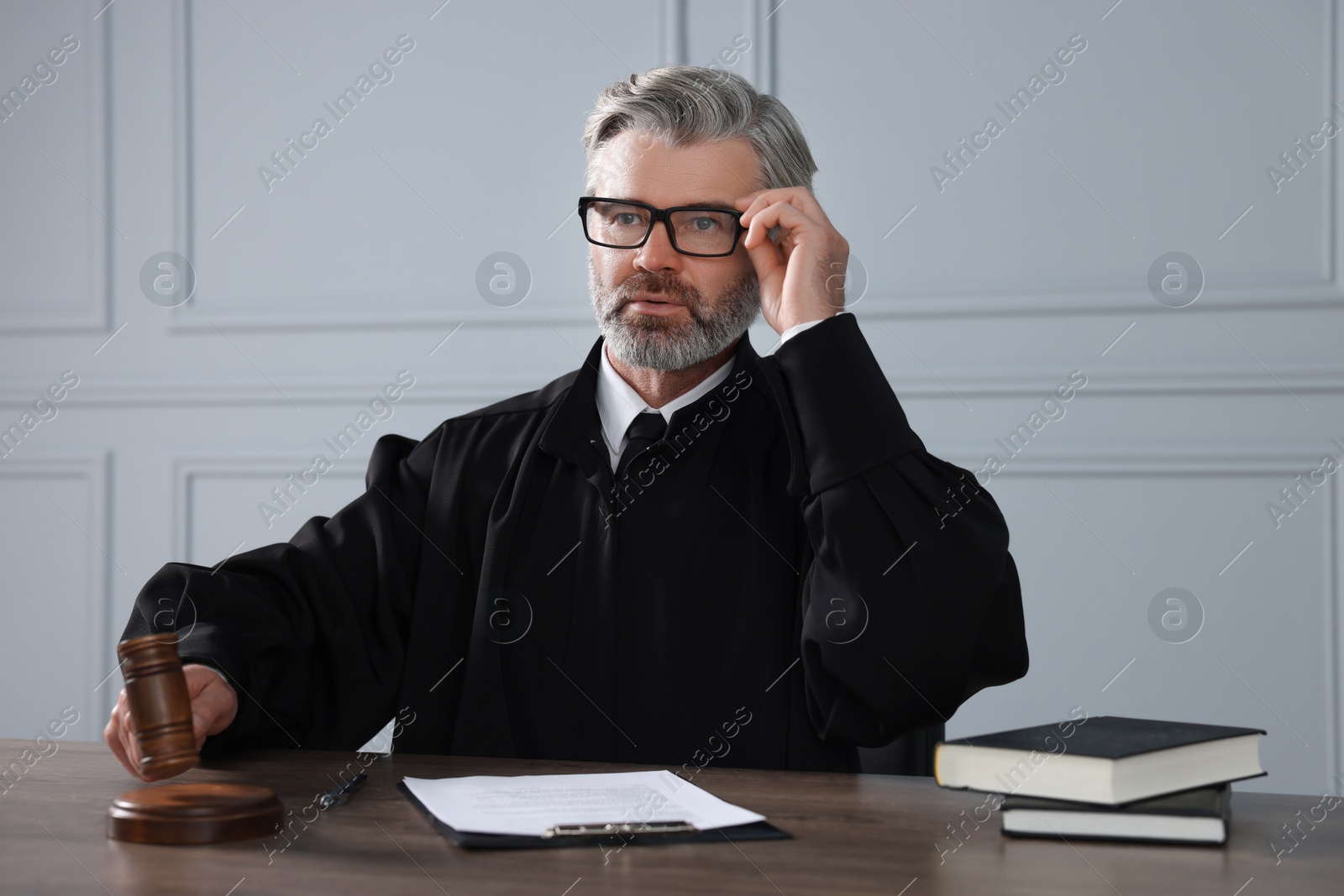 Photo of Judge with gavel, papers and books sitting at wooden table indoors