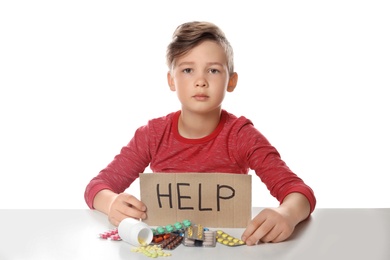 Photo of Little child with many different pills and word Help written on cardboard against white background. Danger of medicament intoxication