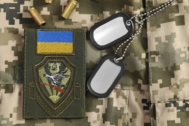 Photo of MYKOLAIV, UKRAINE - SEPTEMBER 26, 2020: Metal military ID tags, bullet shells and Ukrainian army patch on camouflage background, flat lay