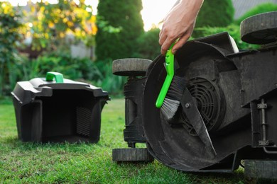 Man cleaning lawn mower with brush in garden, closeup