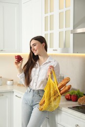 Woman with string bag of baguettes and apple in kitchen
