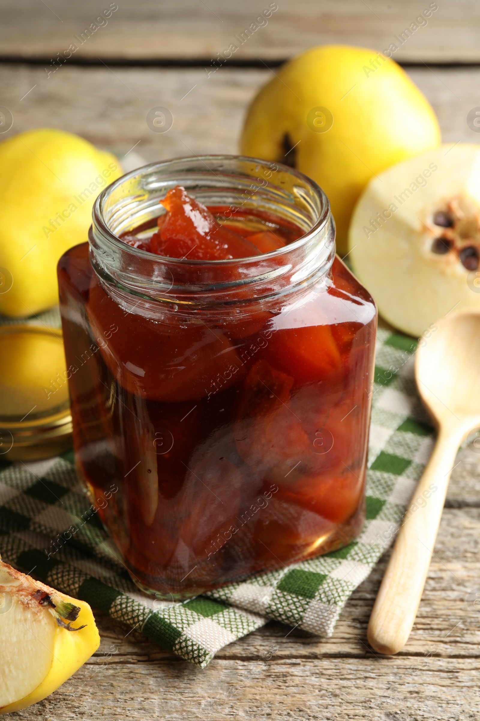 Photo of Tasty homemade quince jam in jar, spoon and fruits on wooden table, closeup