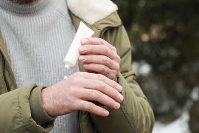 Man applying cream from tube onto hand outdoors, closeup. Winter care