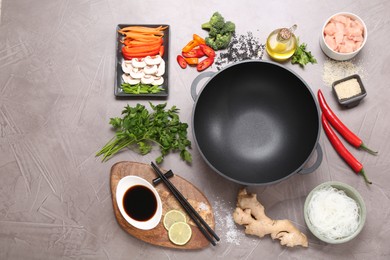 Photo of Wok, chopsticks and different products on grey textured table, flat lay. Space for text