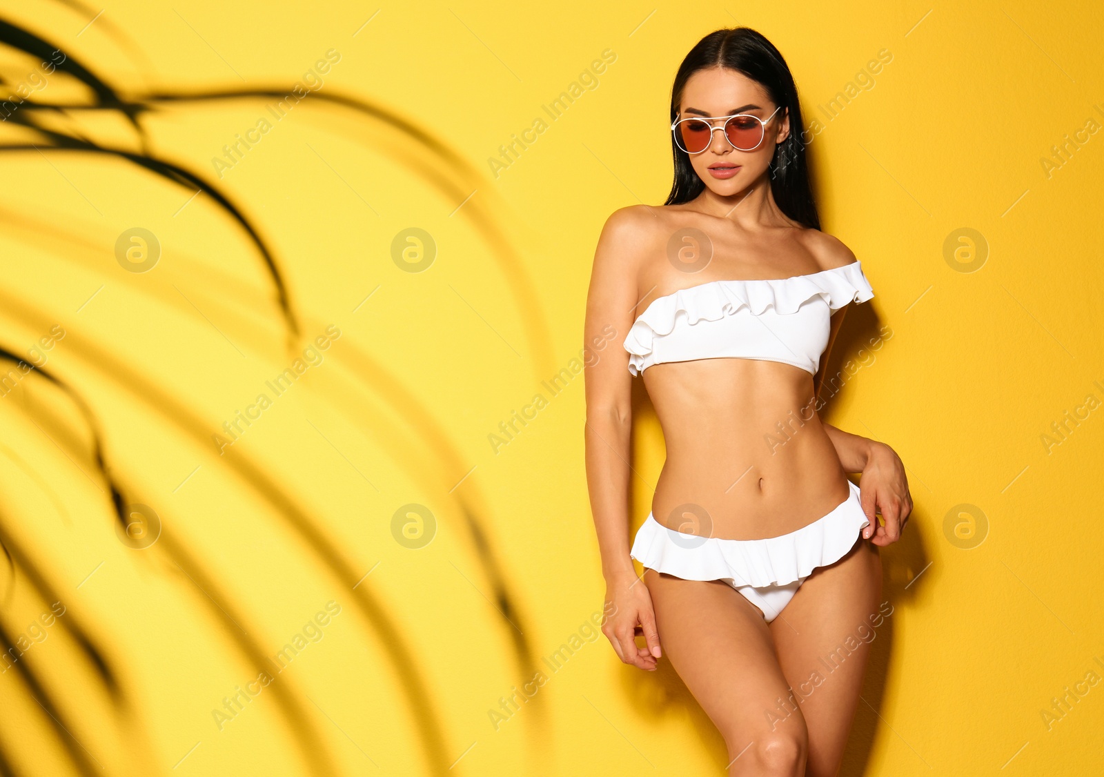 Photo of Beautiful young woman in white bikini with sunglasses on yellow background. Space for text