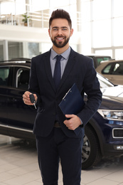 Salesman with key and clipboard in car salon