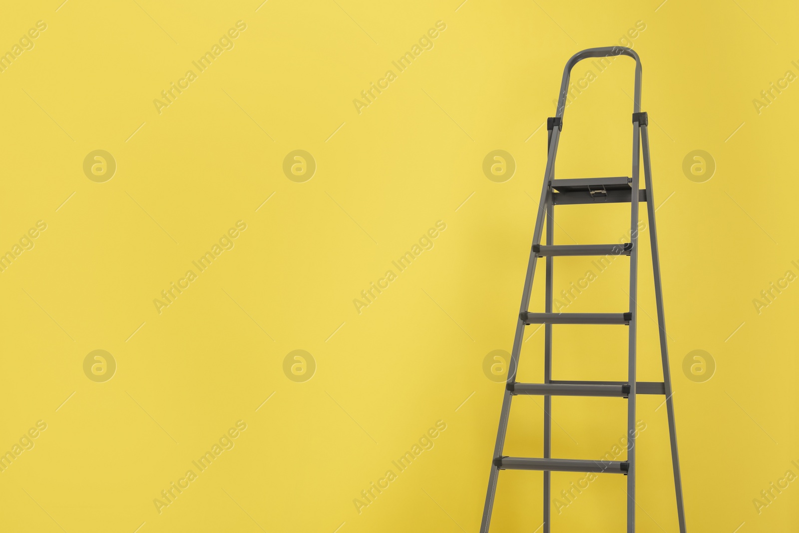 Photo of Metal stepladder on yellow background. Space for text